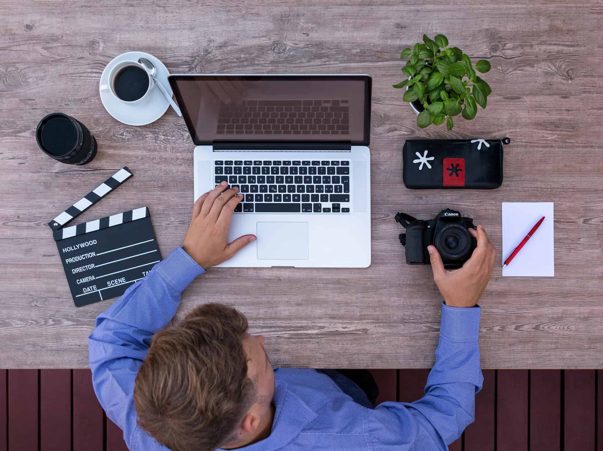 Overhead view of a content creator at a desk with a laptop, Canon camera, clapperboard, and coffee cup