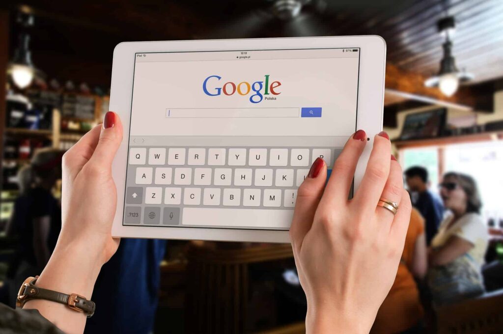 Woman typing on a tablet displaying the Google search homepage with an on-screen keyboard in a cafe setting